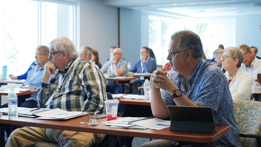 Retirement age men and women sit at tables in a conference room